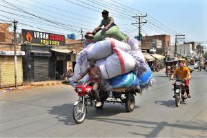 A labourer sitting on luggage loaded on a tricycle loader, while the driver is busy with his cell phone, may cause a mishap