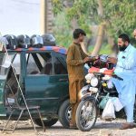 A vendor sells a helmet to a motorcyclist at his roadside setup as citizens purchase safety gear to comply with traffic regulations and avoid fines amid ongoing enforcement drives