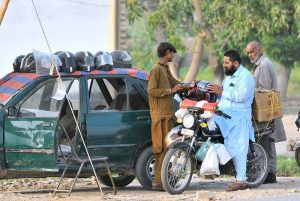 A vendor sells a helmet to a motorcyclist at his roadside setup as citizens purchase safety gear to comply with traffic regulations and avoid fines amid ongoing enforcement drives