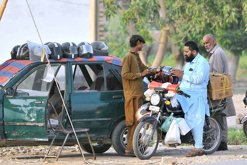 A vendor sells a helmet to a motorcyclist at his roadside setup as citizens purchase safety gear to comply with traffic regulations and avoid fines amid ongoing enforcement drives