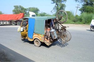 A passenger rickshaw overloaded with passengers and three bicycles moves along 85 Jail Road in violation of traffic regulations.