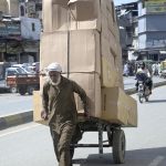 An elderly labourer pulling handcart loaded with luggage to deliver in market at Raja Bazaar