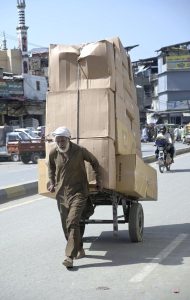 An elderly labourer pulling handcart loaded with luggage to deliver in market at Raja Bazaar