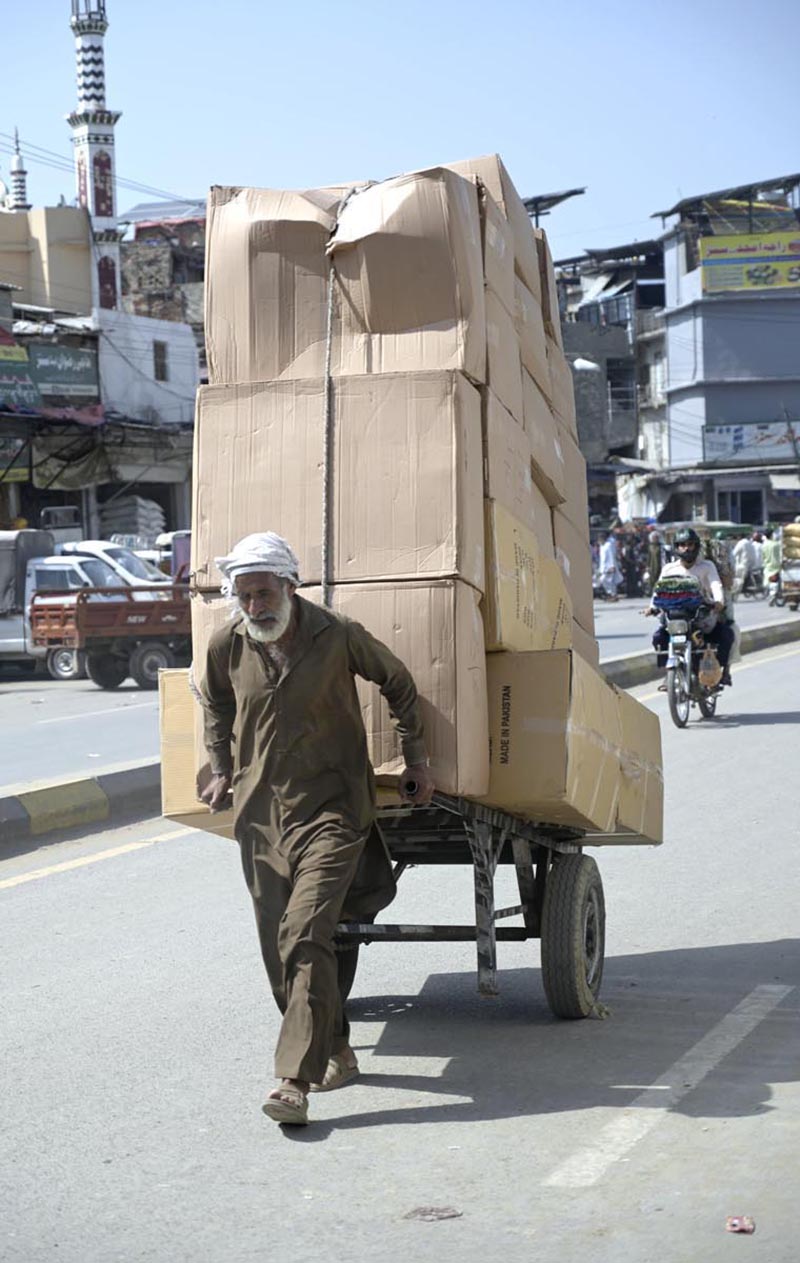 An elderly labourer pulling handcart loaded with luggage to deliver in market at Raja Bazaar