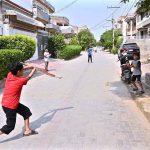 Children are playing cricket in a street at Canal Park