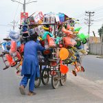 A vendor pushes a cart loaded with children's bicycles and other toys while crossing the road to earn a livelihood
