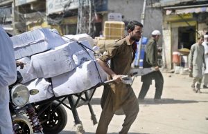 An elderly labourer pulling handcart loaded with luggage to deliver in market at Raja Bazaar
