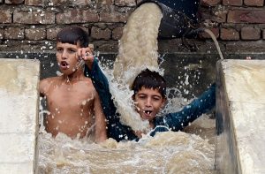 Youngsters cool off by bathing in water from a running tubewell at Hala Naka amid hot weather.