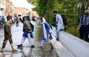 Students wade through rainwater accumulated outside Government Girls High School in Shamsheer Town following rainfall.