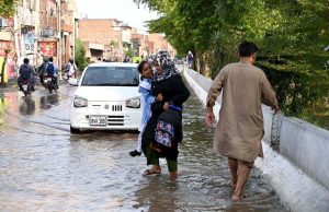 Students wade through rainwater accumulated outside Government Girls High School in Shamsheer Town following rainfall.