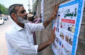 District health workers paste dengue prevention awareness posters on a wall, highlighting precautionary measures to protect people from dengue fever and control the spread of the disease, along Sher Shah Suri Road.