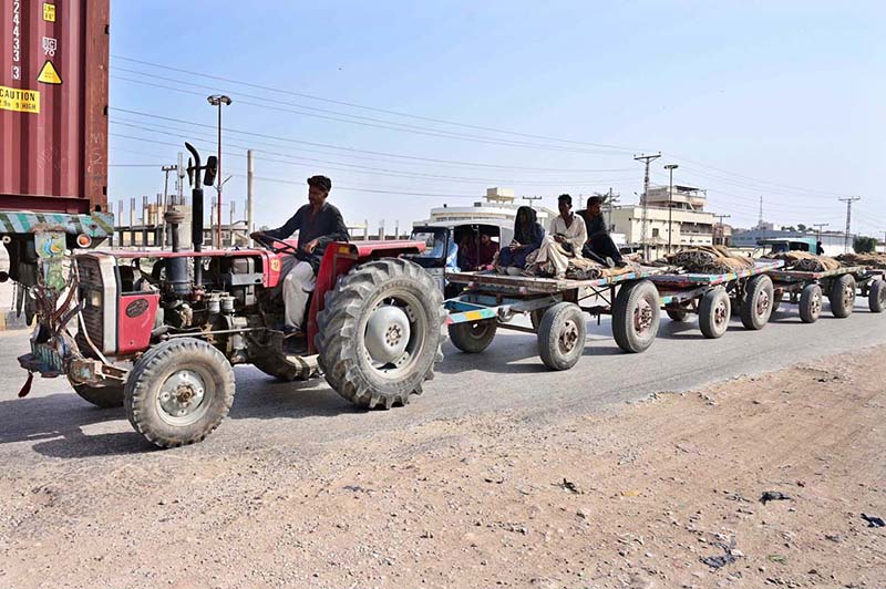 A tractor-trolley carrying a camel cart and other vehicles passes along the Site Area Road