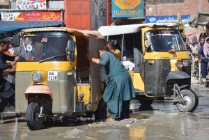 People make efforts to pull out a rickshaw stuck in a roadside ditch along a busy road.