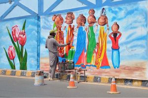 An artist is busy painting a vibrant mural depicting sindhi culture and traditional life at Chungi no 09.