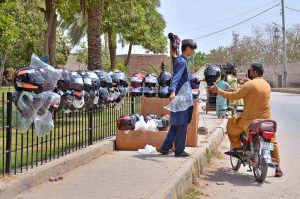 A vendor displays and sells helmets to attract customers at a roadside setup.