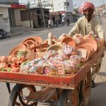 A vendor transports handmade clay pottery on a handcart through a busy street, selling traditional earthenware to local customers