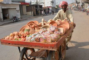A vendor transports handmade clay pottery on a handcart through a busy street, selling traditional earthenware to local customers