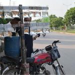 A street vendor displays various colorful ornamental fish for sale in inflated transparent plastic bags, carrying them on his motor bike along a roadside in the city