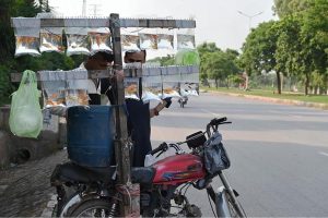 A street vendor displays various colorful ornamental fish for sale in inflated transparent plastic bags, carrying them on his motor bike along a roadside in the city