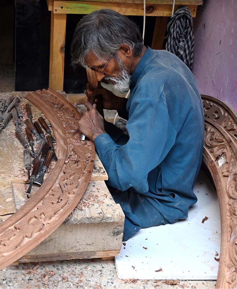 An elderly carpenter carves intricate designs into a wooden piece at his workplace