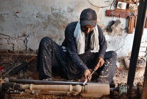 An elderly carpenter carves intricate designs into a wooden piece at his workplace