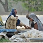 A nomadic woman bakes bread over a traditional stove outside her makeshift tent while sharing a light moment with a family member