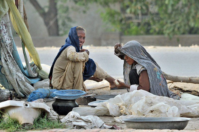 A nomadic woman bakes bread over a traditional stove outside her makeshift tent while sharing a light moment with a family member