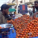 A vendor selling fresh seasonal Japanese fruit (persimmons) from a handcart by the roadside in the city