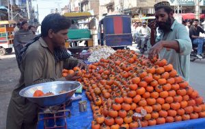 A vendor selling fresh seasonal Japanese fruit (persimmons) from a handcart by the roadside in the city