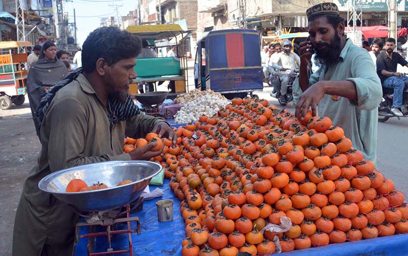A vendor selling fresh seasonal Japanese fruit (persimmons) from a handcart by the roadside in the city