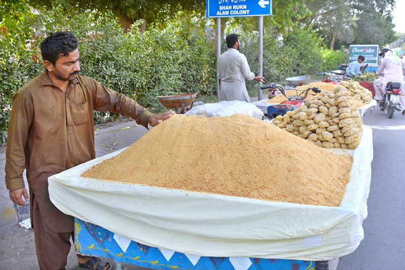 Along a busy road, a roadside vendor displays a large quantity of gur (jaggery) and shakkar (unrefined sugar) to attract customers