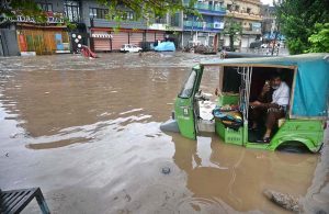 Vehicles navigate through deep floodwater as people wade along a flooded road following heavy monsoon rainfall in Rahimabad area in the City.