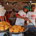 Young vendors prepare and serve freshly fried traditional snacks at a roadside food stall, as they cater to customers in the city