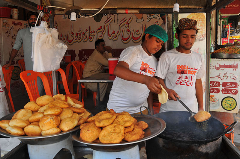 Young vendors prepare and serve freshly fried traditional snacks at a roadside food stall, as they cater to customers in the city