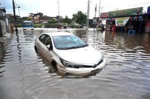 Vehicles navigate through deep floodwater as people wade along a flooded road following heavy monsoon rainfall in Rahimabad area in the City.