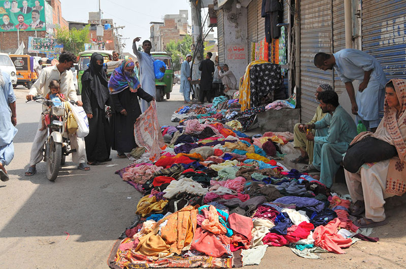 Vendors display colourful garments along a roadside to attract customers, while shoppers browse through the clothes at a busy market