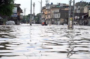 Vehicles navigate through deep floodwater as people wade along a flooded road following heavy monsoon rainfall in Rahimabad area in the City.