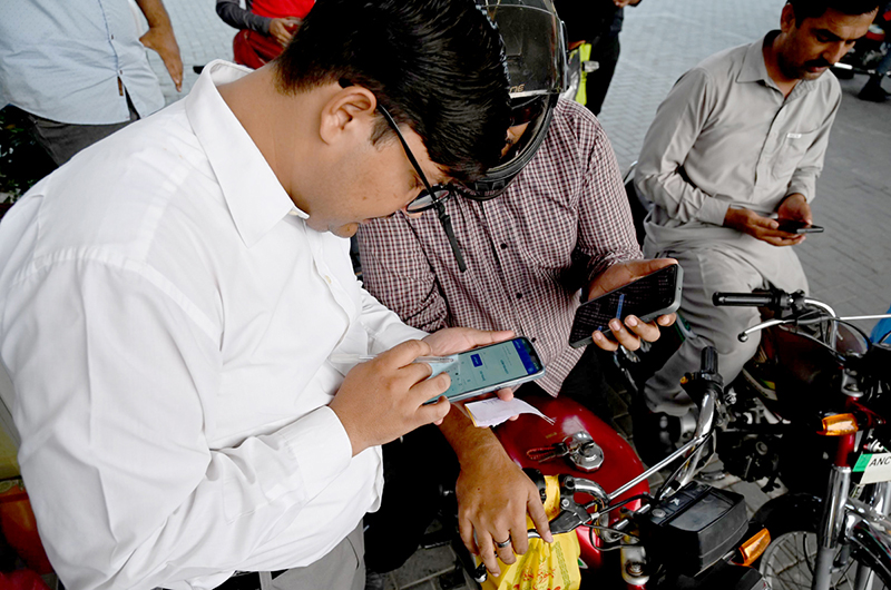 A petrol pump employee verifies a token number from mobile message presented by a motorist to confirm eligibility for subsidized fuel under the Prime Minister’s petrol relief package