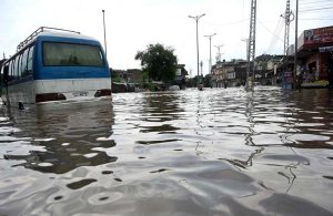 Vehicles navigate through deep floodwater as people wade along a flooded road following heavy monsoon rainfall in Rahimabad area in the City.