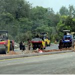Heavy road rollers compact freshly laid asphalt at the Park Road Underpass project site, as construction machinery including Dynapac and Sakai rollers work alongside labourers to complete the carpeting of the road surface in the project's final phase