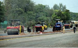 Heavy road rollers compact freshly laid asphalt at the Park Road Underpass project site, as construction machinery including Dynapac and Sakai rollers work alongside labourers to complete the carpeting of the road surface in the project's final phase