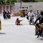 A woman begs on the roadside in front of the Chandka Medical College gate