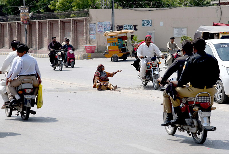 A woman begs on the roadside in front of the Chandka Medical College gate