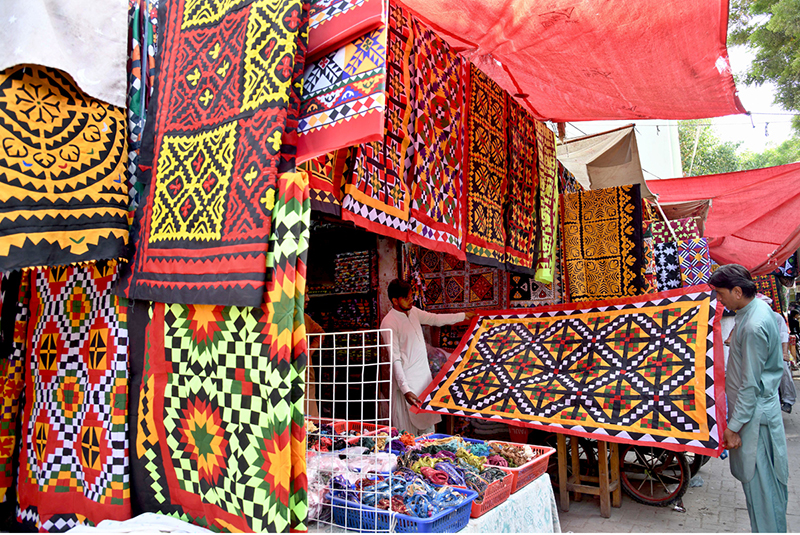 Vendors display colorful handmade traditional patchwork bed sheets for a customer at his shop