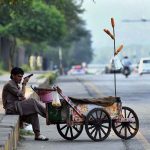 A street corn vendor listens his mobile phone while waiting for customers to sell roasted corn cobs along Faisal Avenue