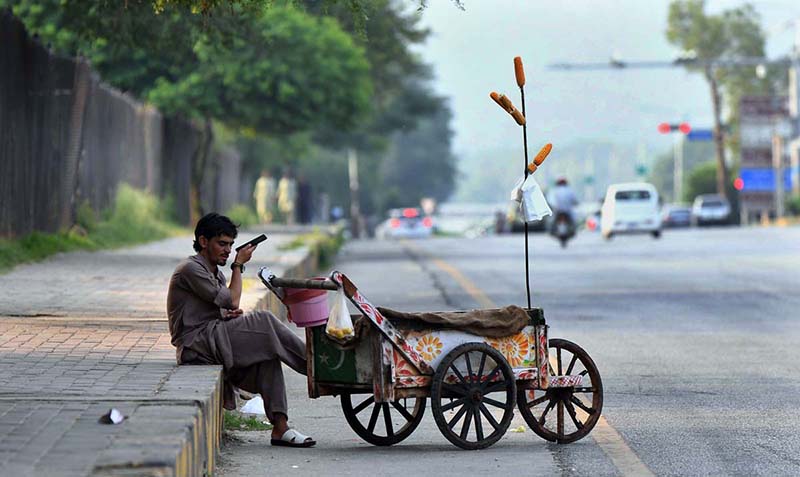 Report: A street corn vendor listens his mobile phone while waiting for customers to sell roasted corn cobs along Faisal Avenue
