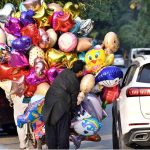 A balloon vendor is trying to persuade a motorist to buy a balloon at Jinnah Supermarket