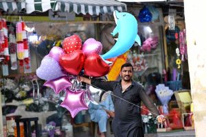 A balloon vendor is trying to persuade a motorist to buy a balloon at Jinnah Supermarket