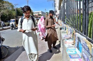 Students browse books from display by a street vendor for sale along the wall on roadside of an official building near Jinnah Road.