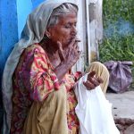 An elderly woman busy is smoking a cigarette near Jinnah Bagh Chowk